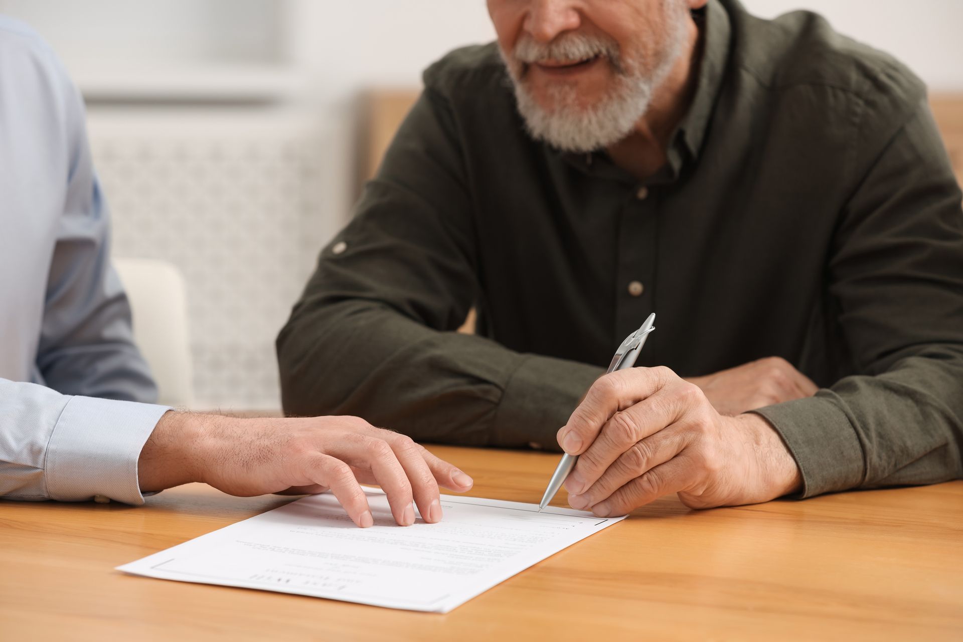 Two men at a table; one signing a document. The setting appears to be indoors.
