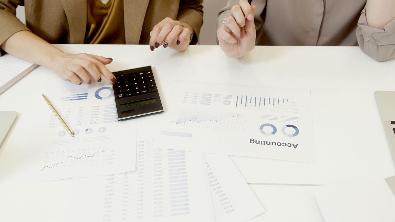 Hands reviewing documents and a calculator on a white desk during a financial meeting