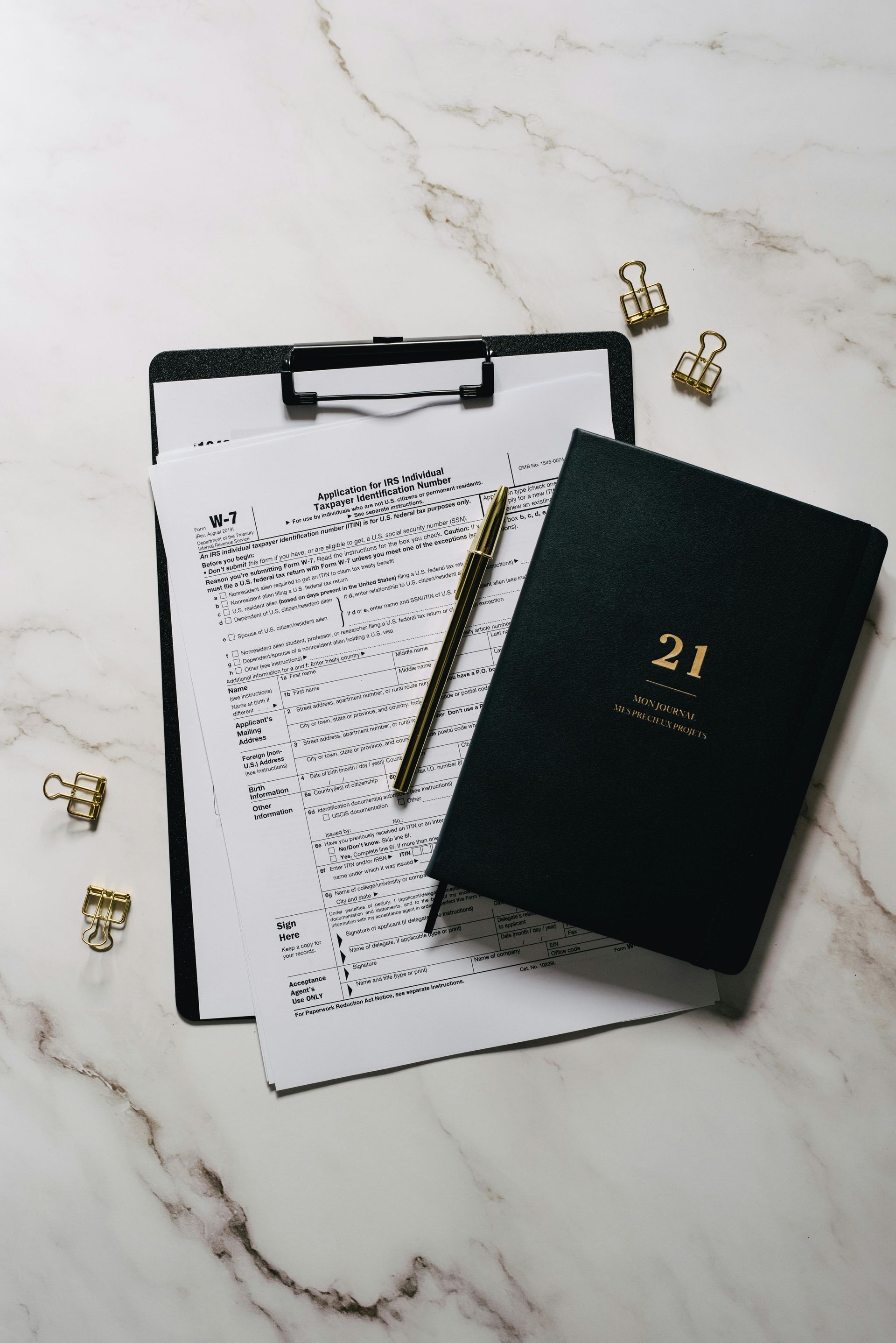Music sheet, clipboard, pen, and black 21 planner on a white marble surface
