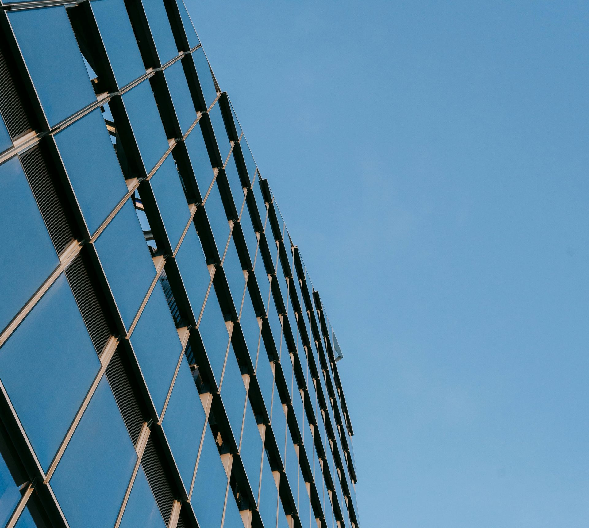 A low-angle view of a modern glass skyscraper with a repeating grid pattern against a clear blue sky.