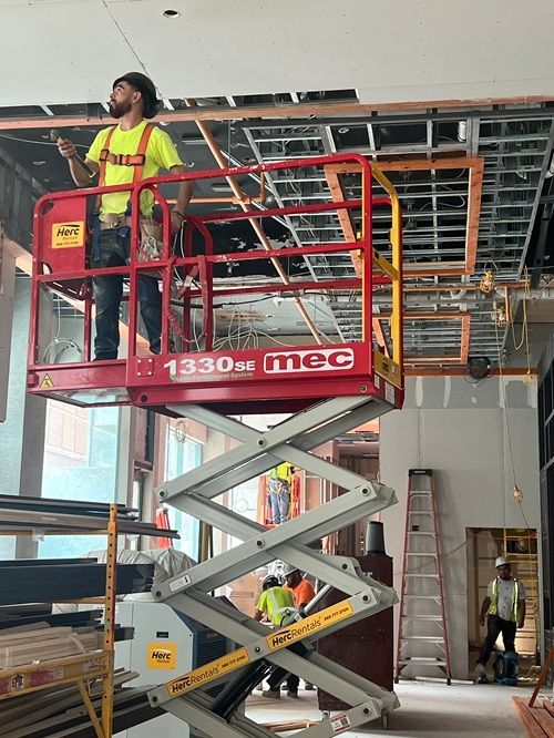 A man is standing on a scissor lift in a building under construction.