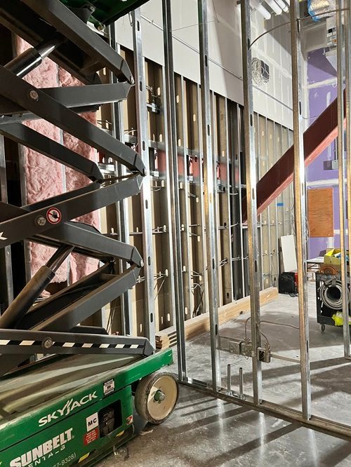 A green scissor lift is in a building under construction.