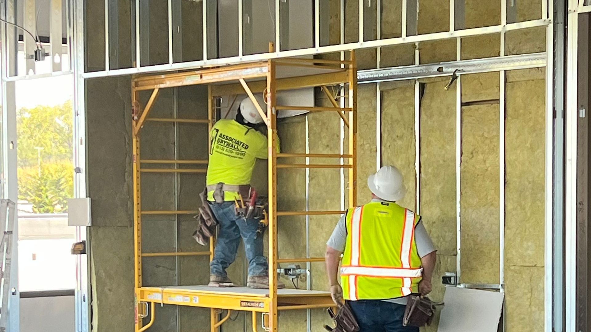Two construction workers are working on a wall in a building under construction.