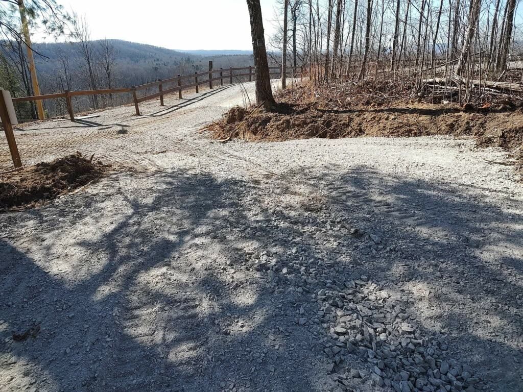 A gravel path leads to a wooden fence overlooking a scenic mountain view under a clear sky.