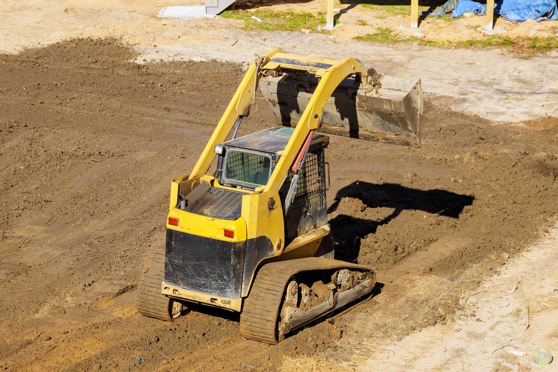 A yellow compact track loader operates on a dirt construction site.
