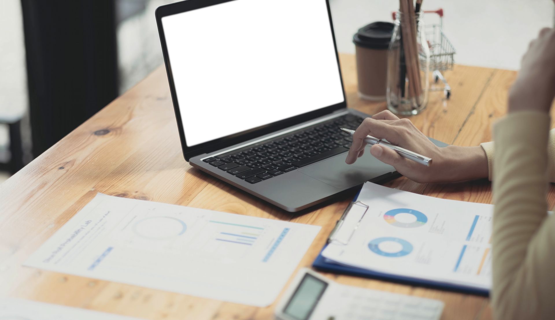 Person reviewing printed charts beside an open laptop on a wooden desk