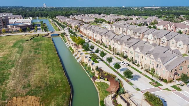 Aerial view of a canal beside rows of beige suburban townhouses and a grassy field
