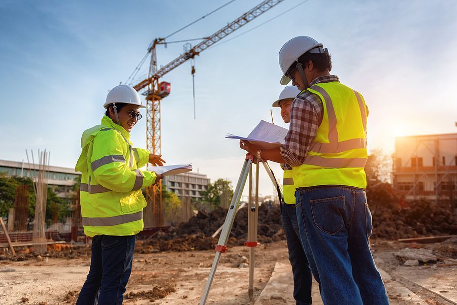 Two construction workers in safety vests and hard hats reviewing plans at a building site