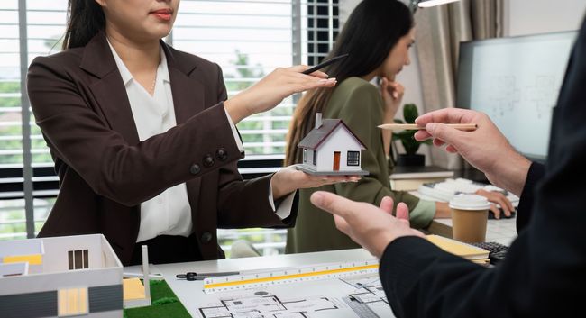 Team reviewing a small house model and floor plans in a bright office meeting room