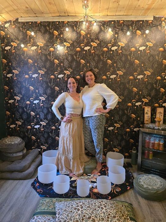 two women posing in the middle of sound bowls two women standing in front of a mushroom wall with crystal sound bowls around them