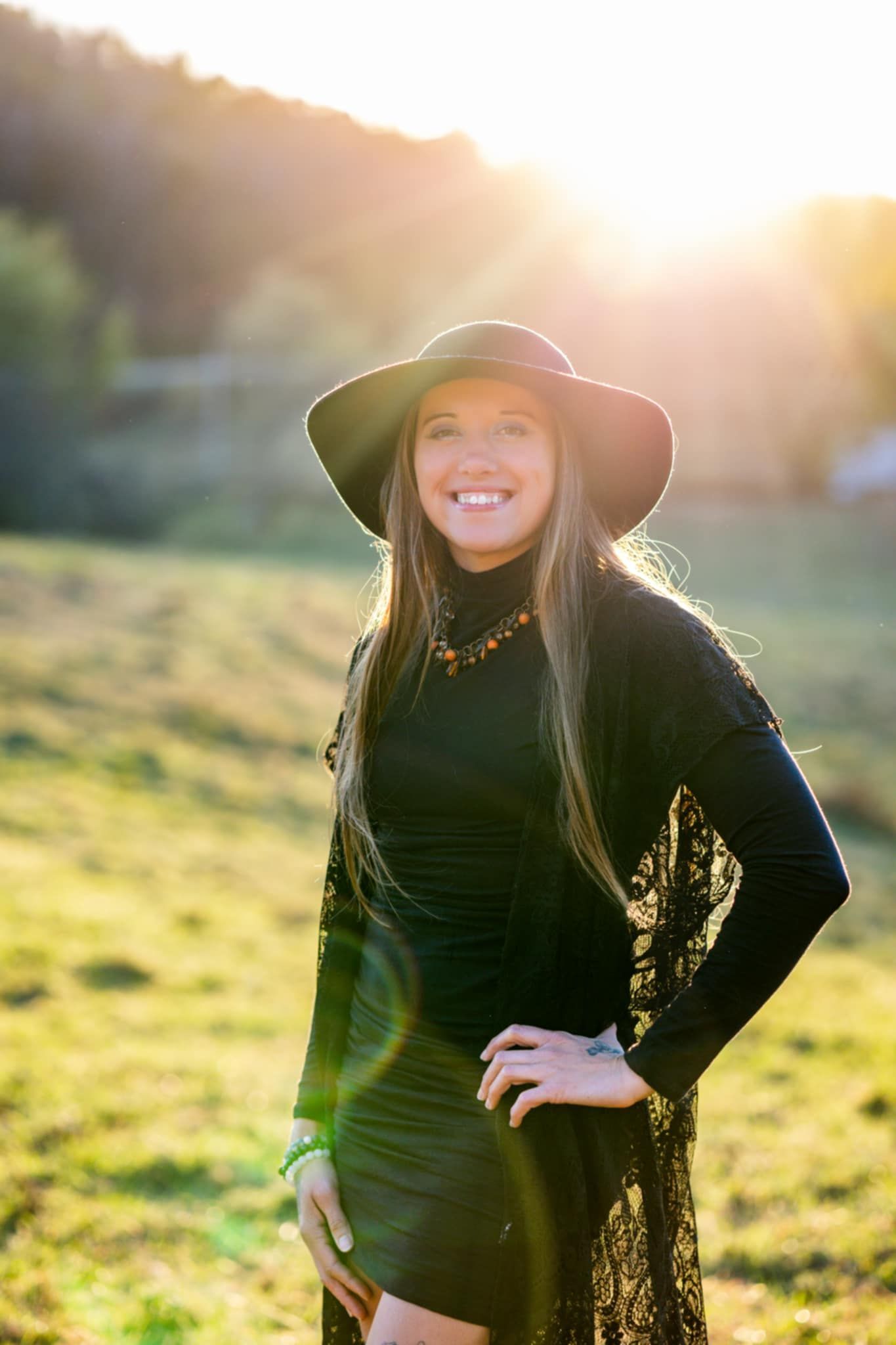 A smiling woman in a black dress with a black hat and a lace cover with the sun shining behind her in a green field. A smiling woman in a black dress with a black hat and a lace cover with the sun shining behind her in a green field.