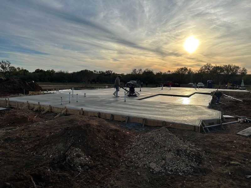 Crew power-troweling a new concrete foundation slab at sunset near San Antonio, TX