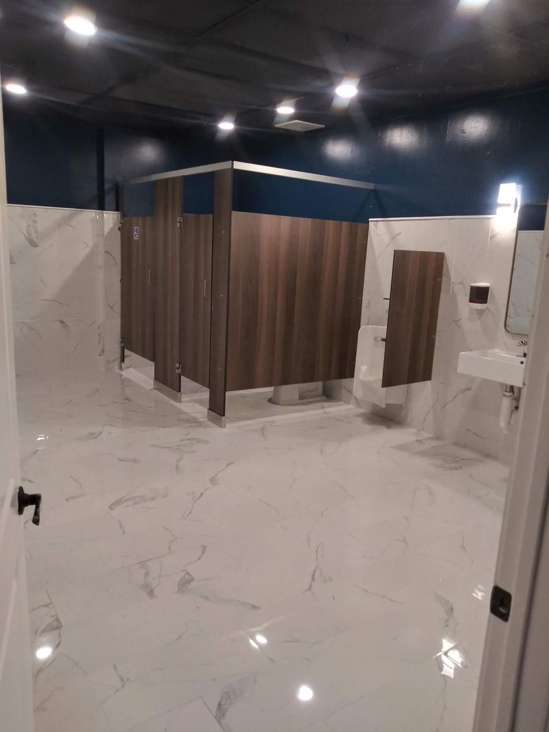 Finished commercial restroom with marble-look tile and stall partitions