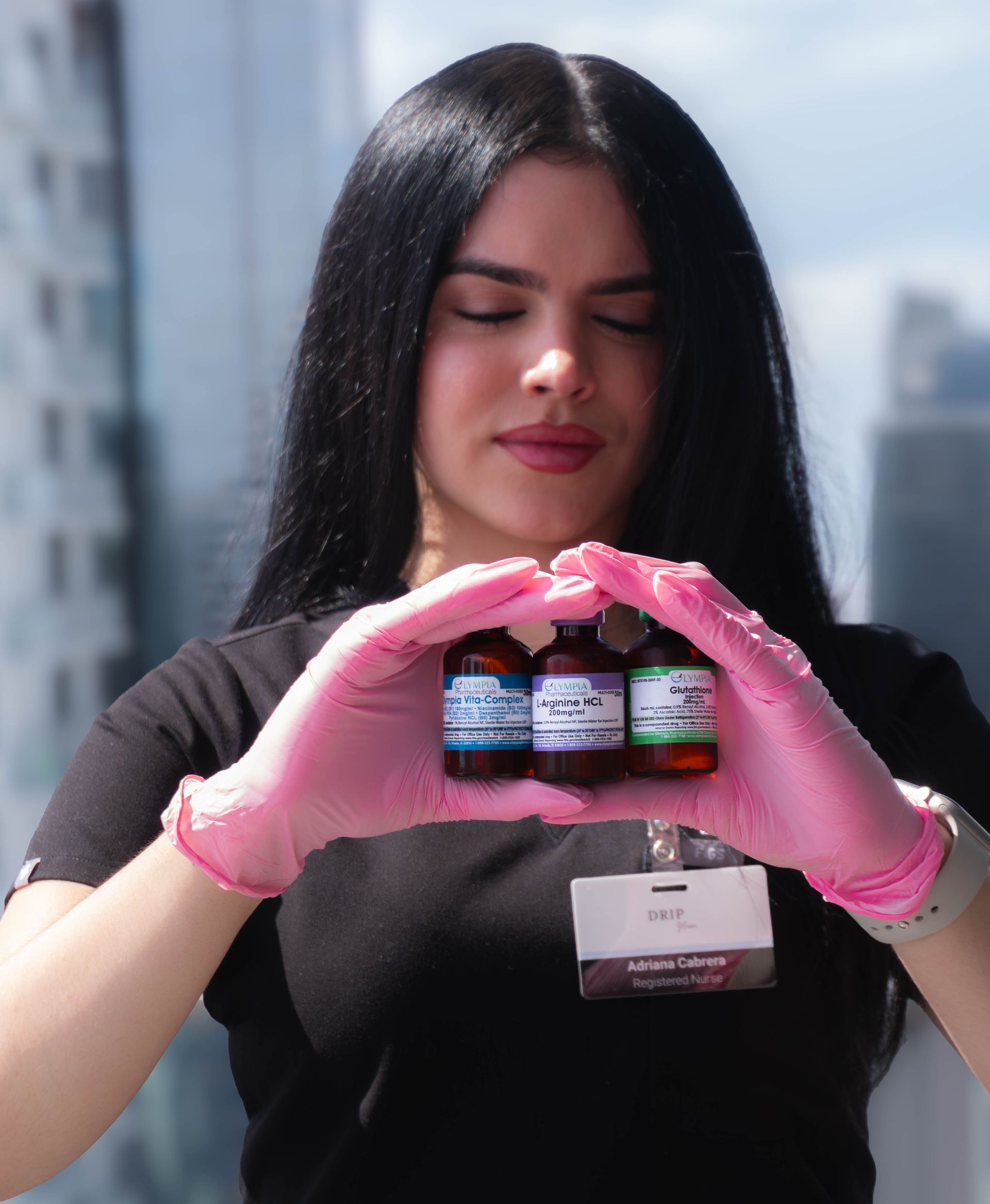 Woman in pink gloves holds three small bottles, city backdrop.