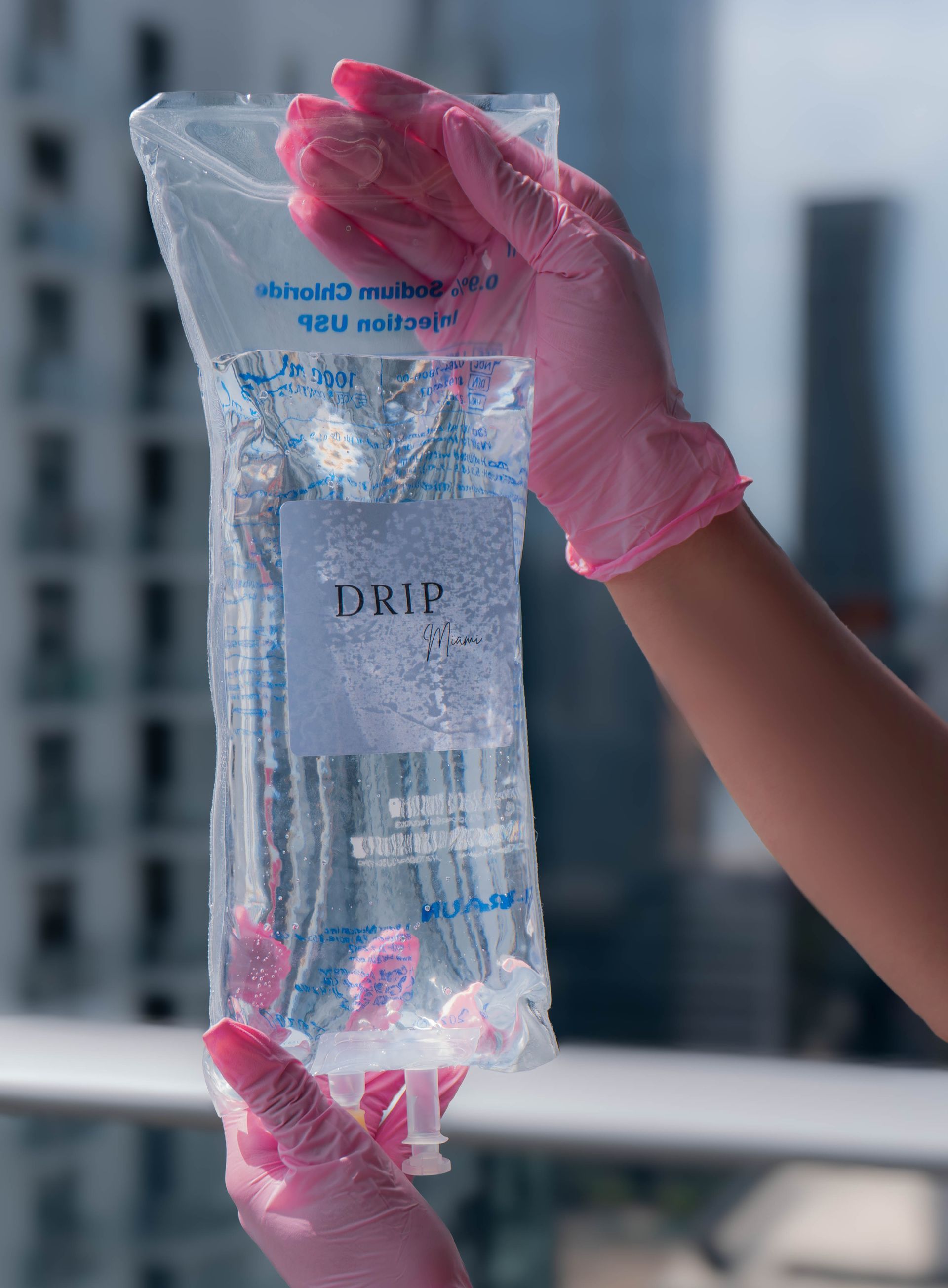 Hands in pink gloves holding a clear IV bag labeled