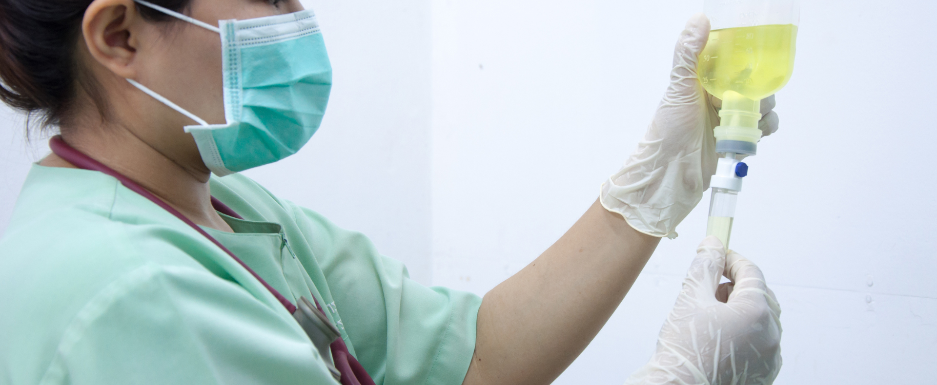 Masked healthcare worker holding IV bag and syringe in a clinical setting