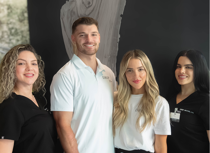 Four smiling people posing in front of a dark wall. 