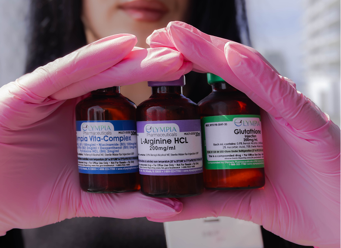 Person in pink gloves holds three vials labeled with pharmaceutical ingredients.