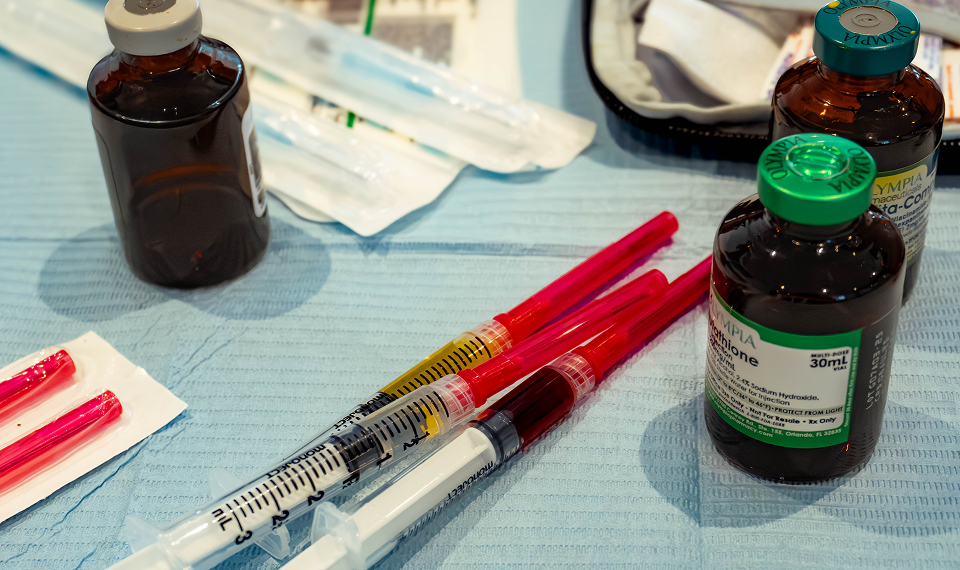 Syringes and vials with red and brown liquids on a blue table, possibly medical supplies.