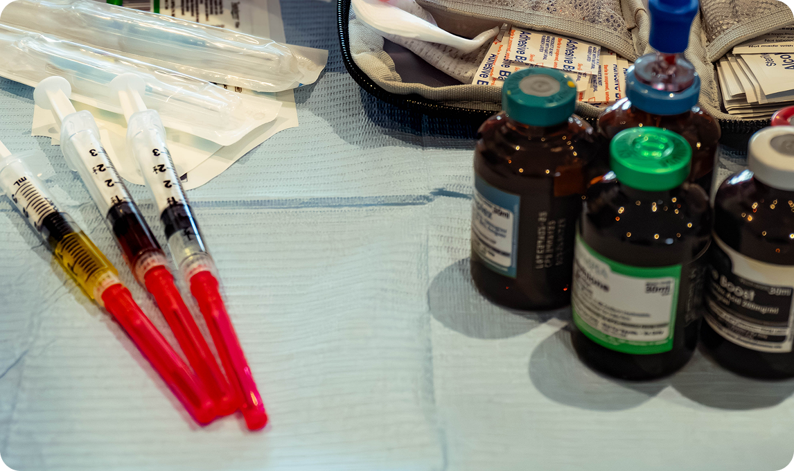 Syringes filled with liquid, next to medicine vials on a light blue surface.