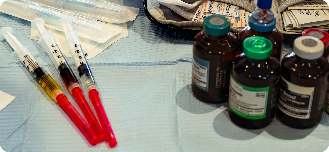 Syringes filled with liquid and bottles with colored caps on a light blue surface.