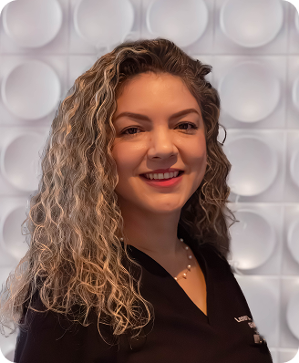 Woman with curly brown hair smiles, wearing a black top, in front of a white textured wall.