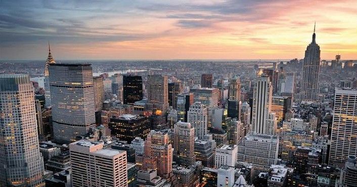 Veduta aerea dello skyline di una città al tramonto, con alti edifici sotto un cielo rosa-arancio.