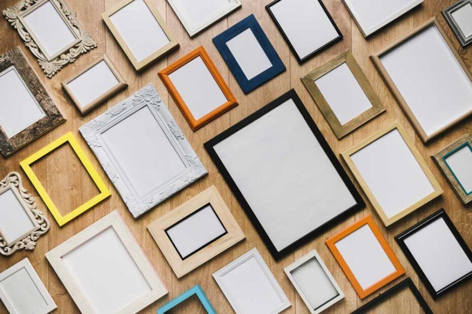 Diverse cornici vuote di colore bianco, oro, blu e arancione, disposte su una superficie di legno.