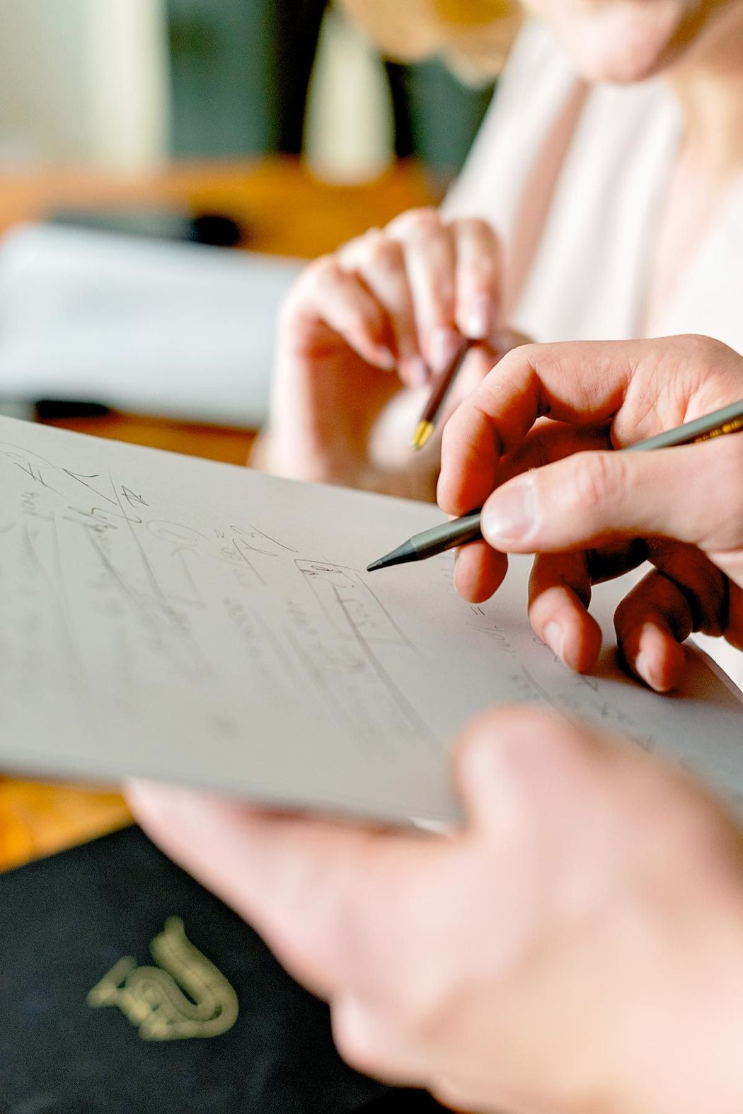Mani che disegnano su carta con una matita in un ambiente interno caldo.
