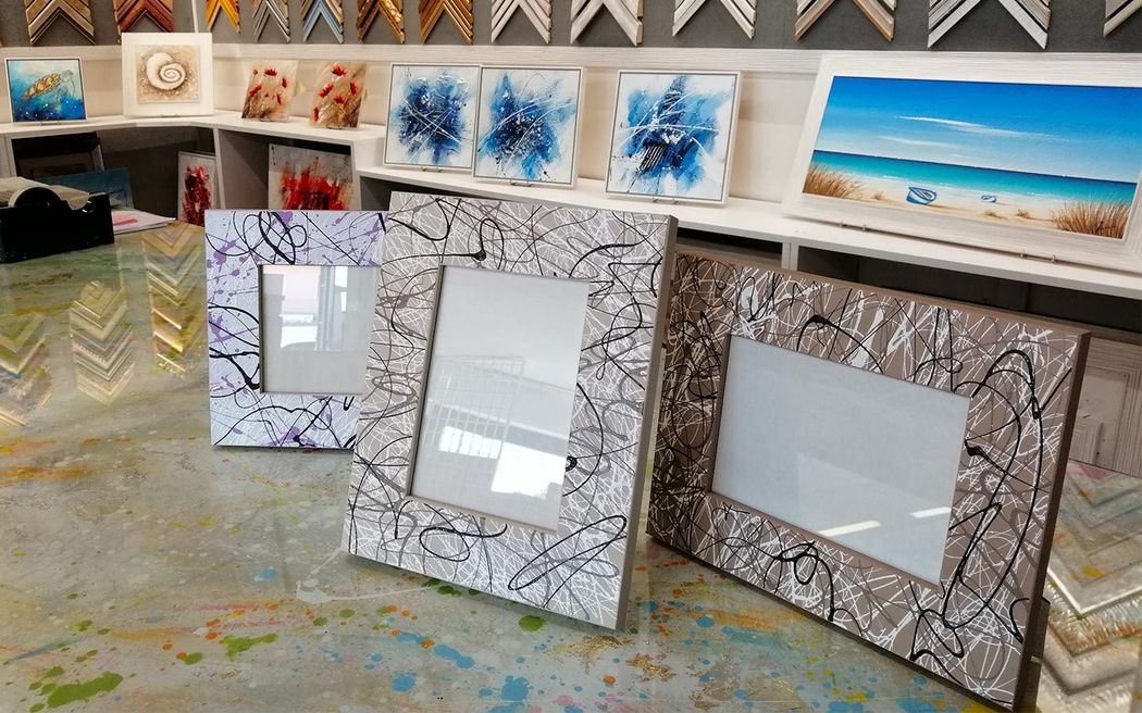 Esposizione di specchi decorativi incorniciati e opere d'arte da parete in un negozio di artigianato, con dipinti di oceano blu su uno scaffale.