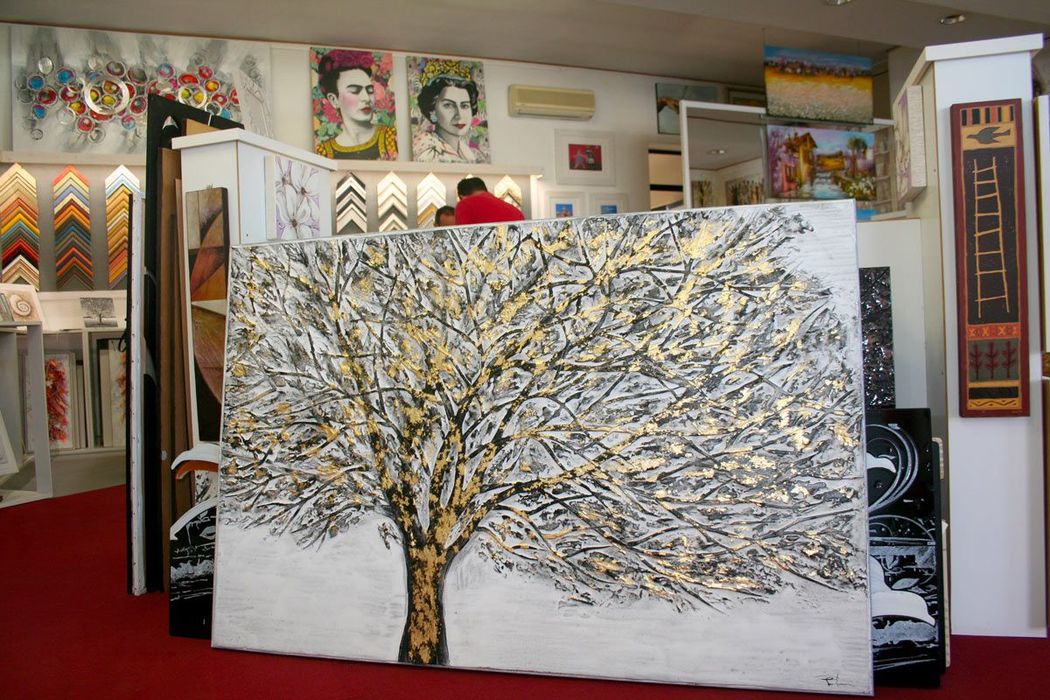 Un grande dipinto raffigurante un albero su sfondo bianco, esposto in uno studio d'arte e circondato da altre opere.