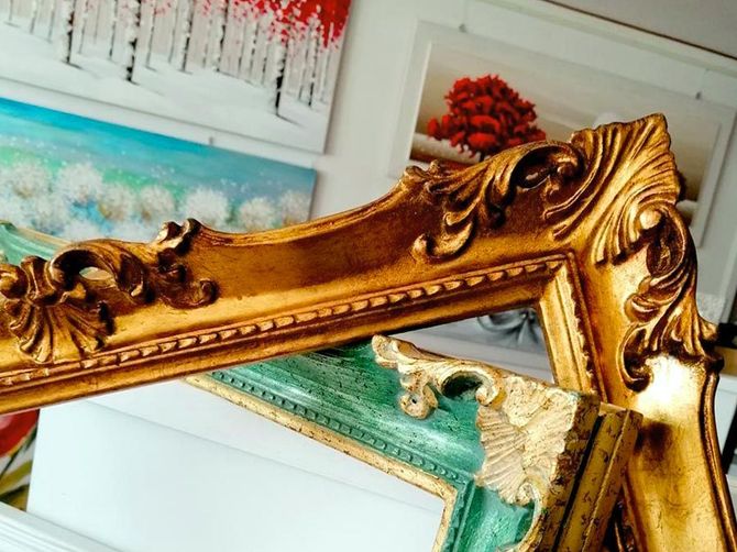 Elegante cornice dorata decorata con motivi floreali, appesa in una stanza con un'opera d'arte astratta alla parete.