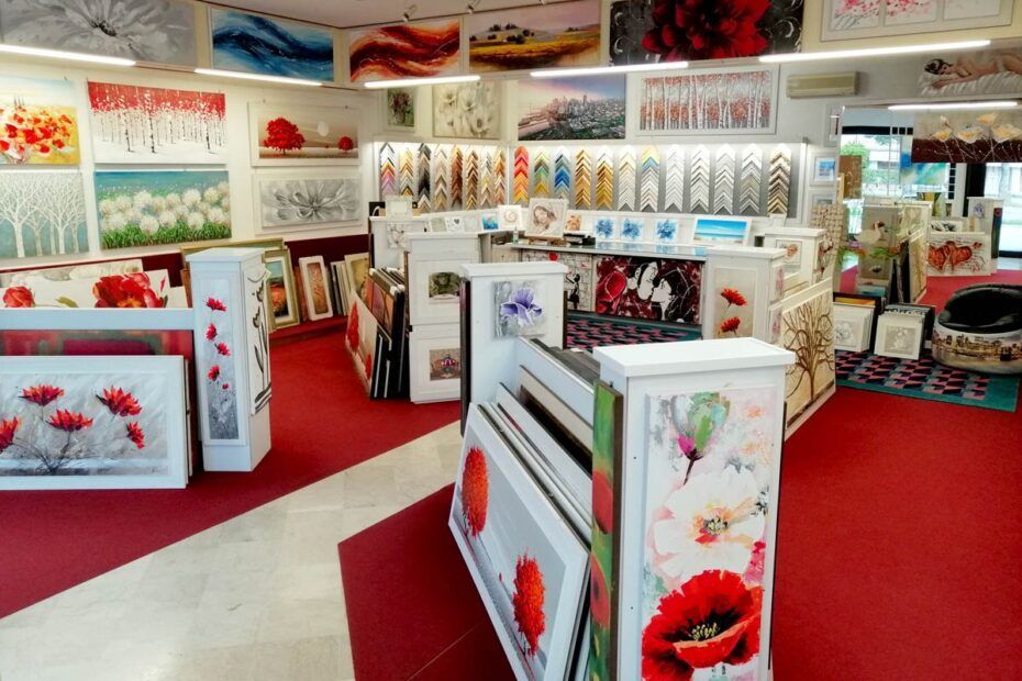 Opere floreali decorative esposte in una luminosa sala espositiva con tappeto rosso e supporti espositivi bianchi.