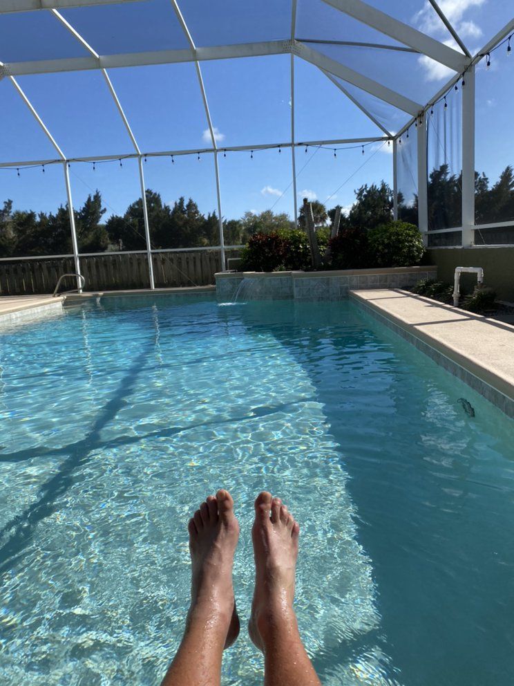 Feet resting by a sunlit outdoor pool under a screened enclosure