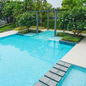 Modern outdoor swimming pool with turquoise water, stepping stones, and lush green landscaping