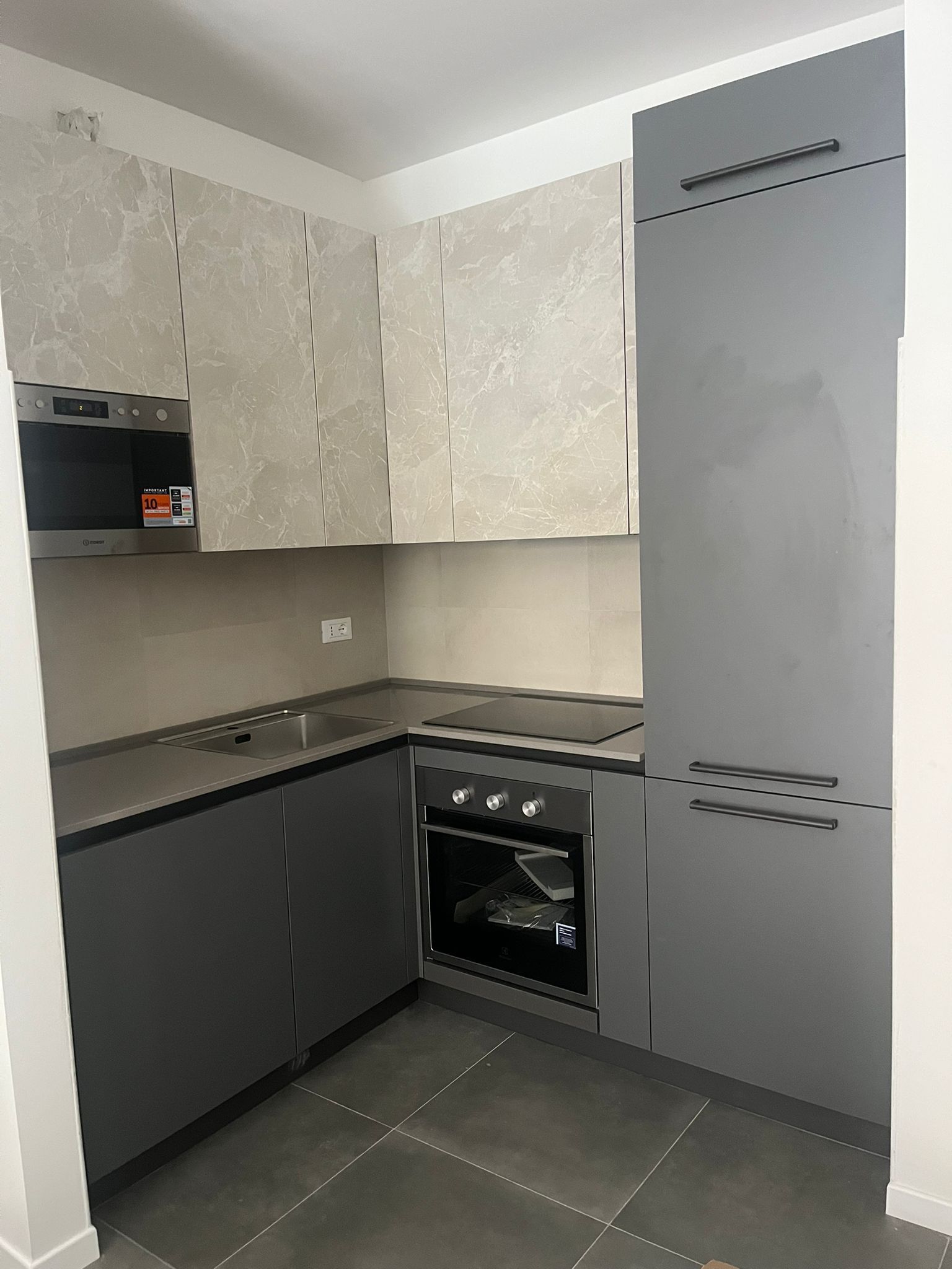 Una moderna cucina a L con mobili base grigio antracite, forno a incasso e pensili con decorazioni chiare.