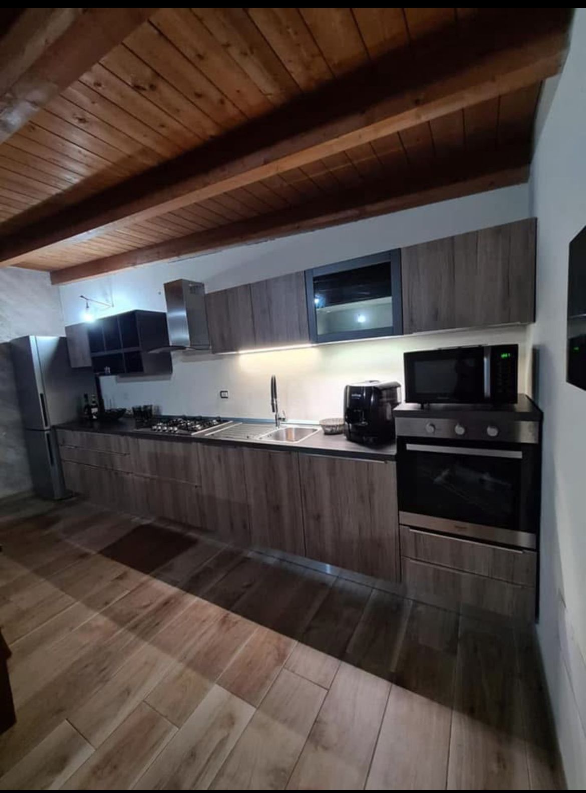 Cucina moderna con mobili in legno, elettrodomestici in acciaio inossidabile, paraschizzi piastrellato e soffitto con travi a vista.
