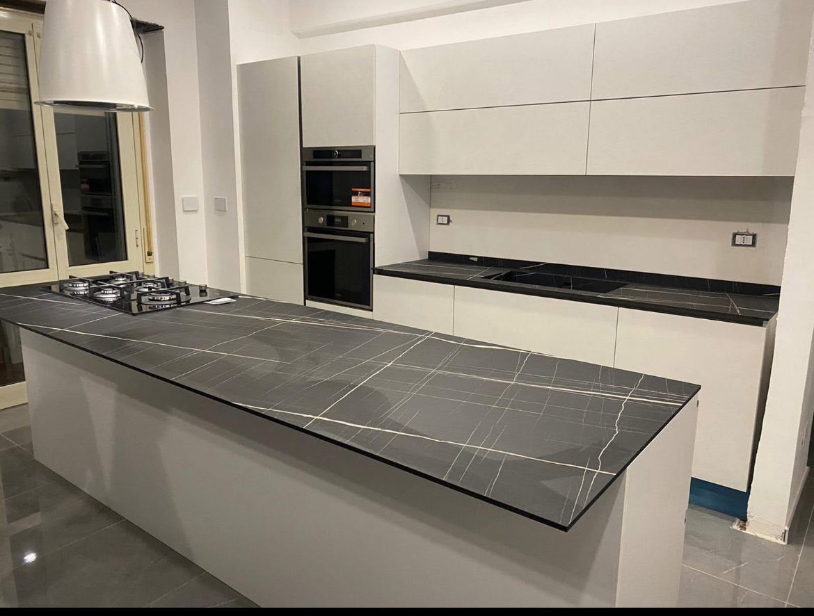 Cucina moderna con isola grigia, ripiani con motivo in pietra scura, mobili bianchi e forni a incasso.