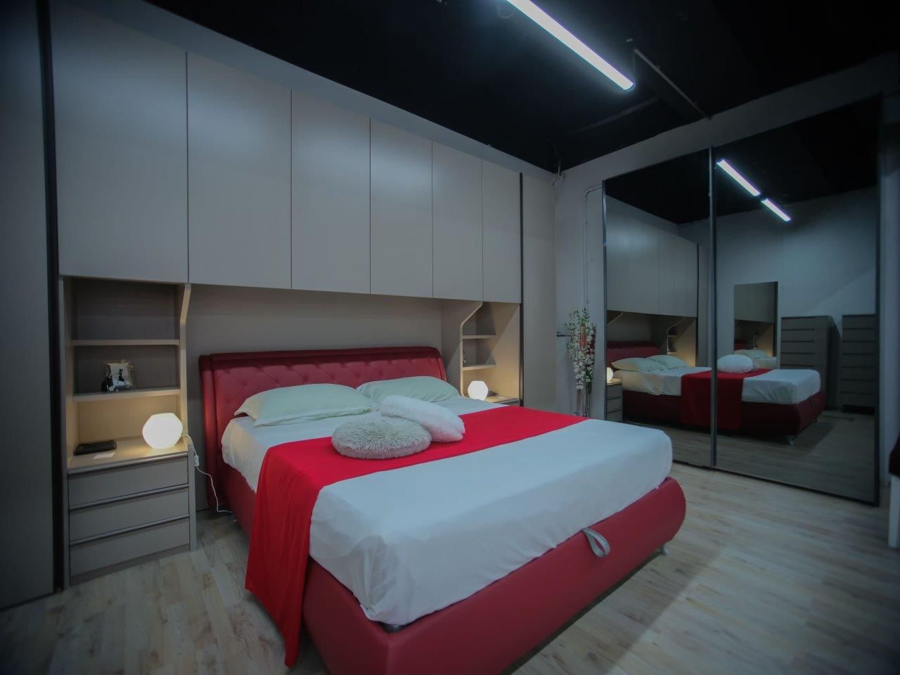 Un letto rosso con lenzuola bianche al centro di una camera da letto con armadi beige a tutta altezza e un grande armadio con ante a specchio.