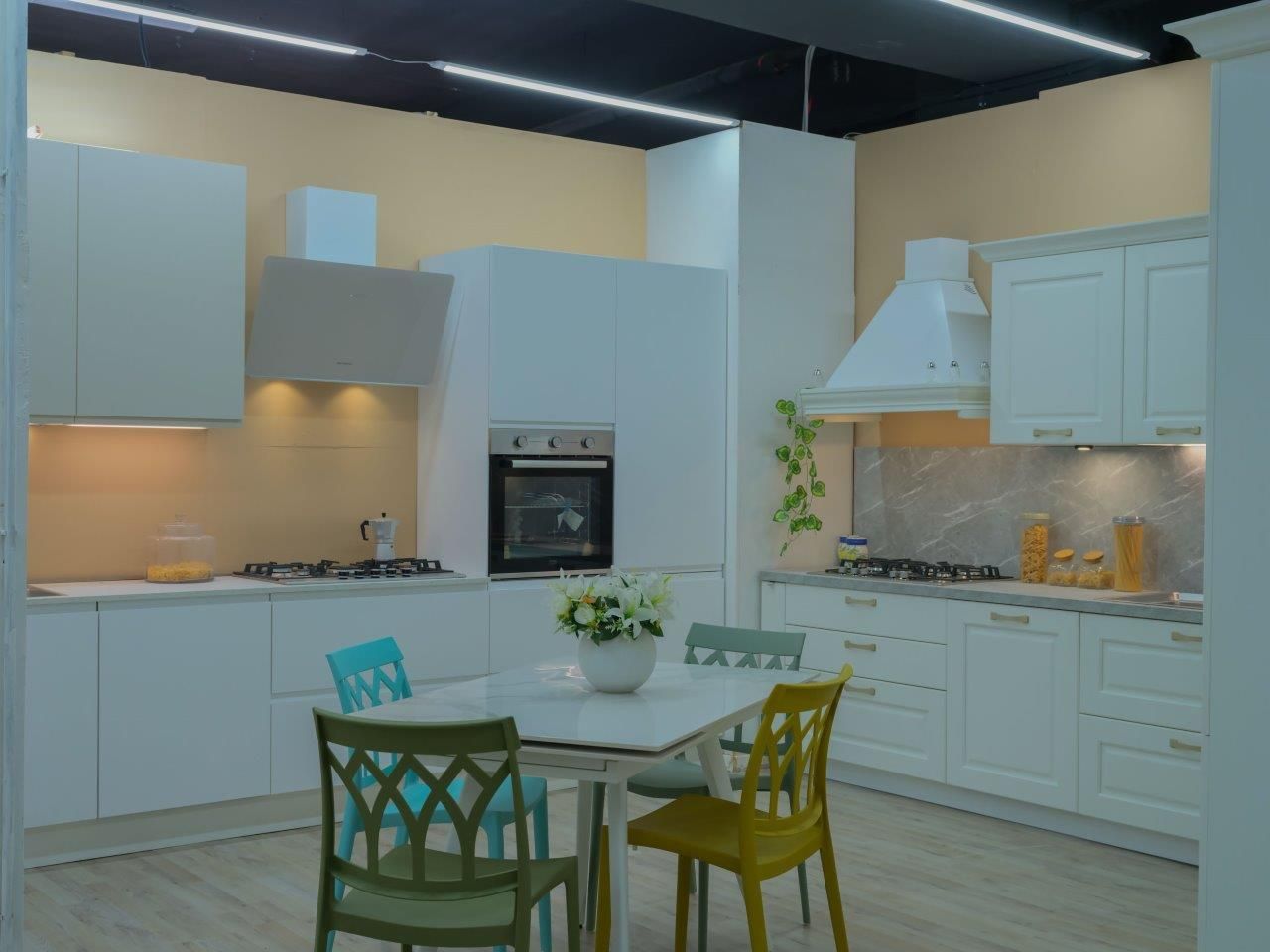 Una moderna cucina a vista con mobili bianchi, un tavolo da pranzo centrale e quattro sedie colorate.