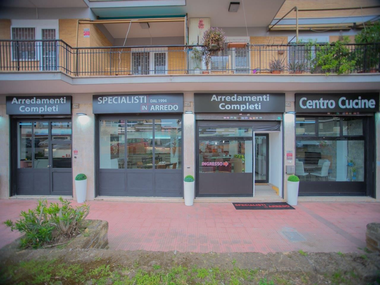 Lungo un marciapiede lastricato si susseguono diverse attività commerciali, tra cui Arredamenti Completi e Centro Cucine.