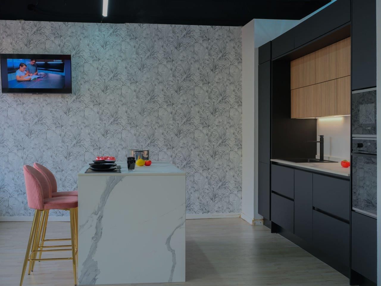 Una cucina moderna con isola centrale con piano in marmo, sgabelli rosa, carta da parati a motivi geometrici e mobili neri opachi.