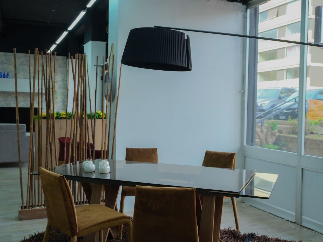 Zona pranzo moderna con tavolo in vetro, quattro sedie color senape, lampada da terra nera e un alto divisorio in bambù.