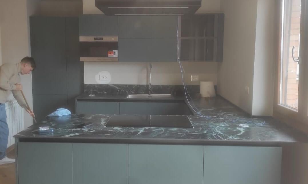Una persona pulisce il piano di lavoro di una cucina moderna con mobili grigio scuro e una superficie effetto marmo.