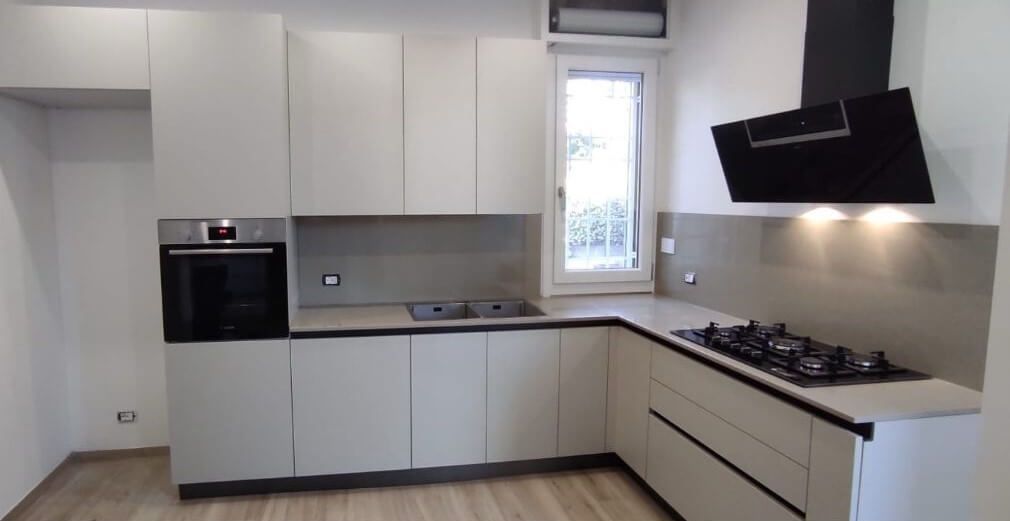 Una cucina moderna con mobili grigio chiaro opaco, forno a incasso, lavello in acciaio inox e cappa aspirante nera.