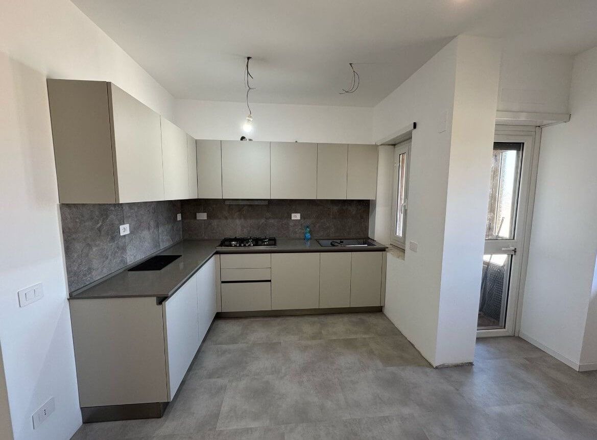 Una moderna cucina a forma di U con mobili chiari, ripiani scuri, paraschizzi piastrellato in grigio e una porta laterale.