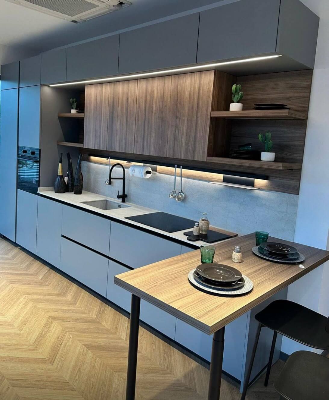 Cucina moderna con mobili color grigio ardesia, dettagli superiori effetto legno, illuminazione sottopensile e bancone per la colazione.