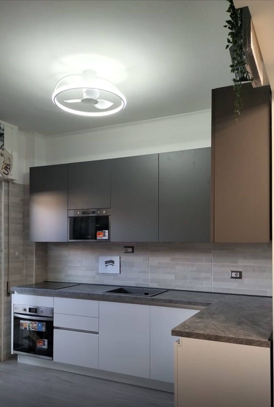 Una cucina moderna con mobili base bianchi, pensili grigi, piano di lavoro in pietra, paraschizzi in piastrelle e lampada a soffitto.