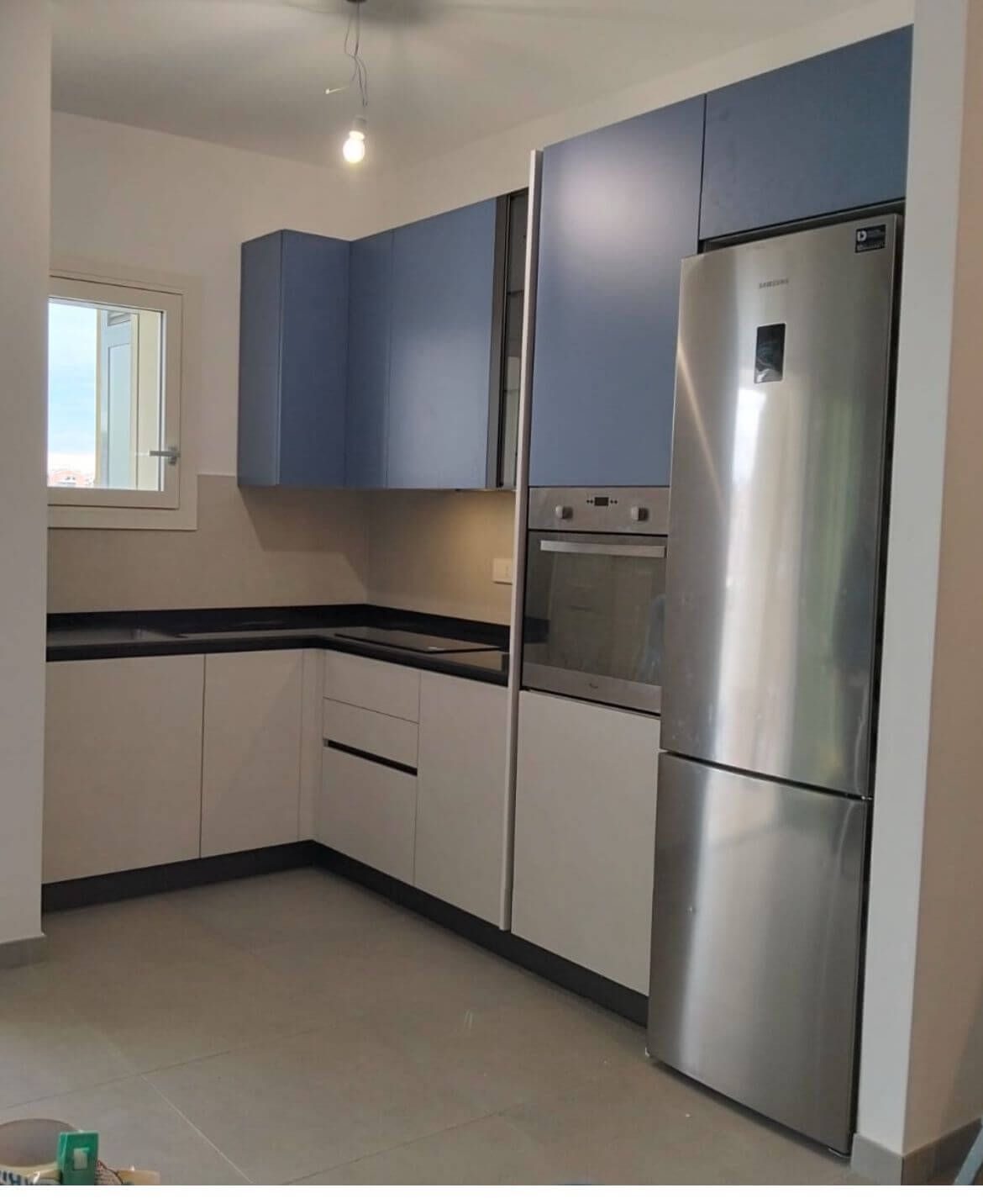 Una moderna cucina a forma di L con pensili bicolore blu, basi chiare, ripiani scuri e un frigorifero a colonna.