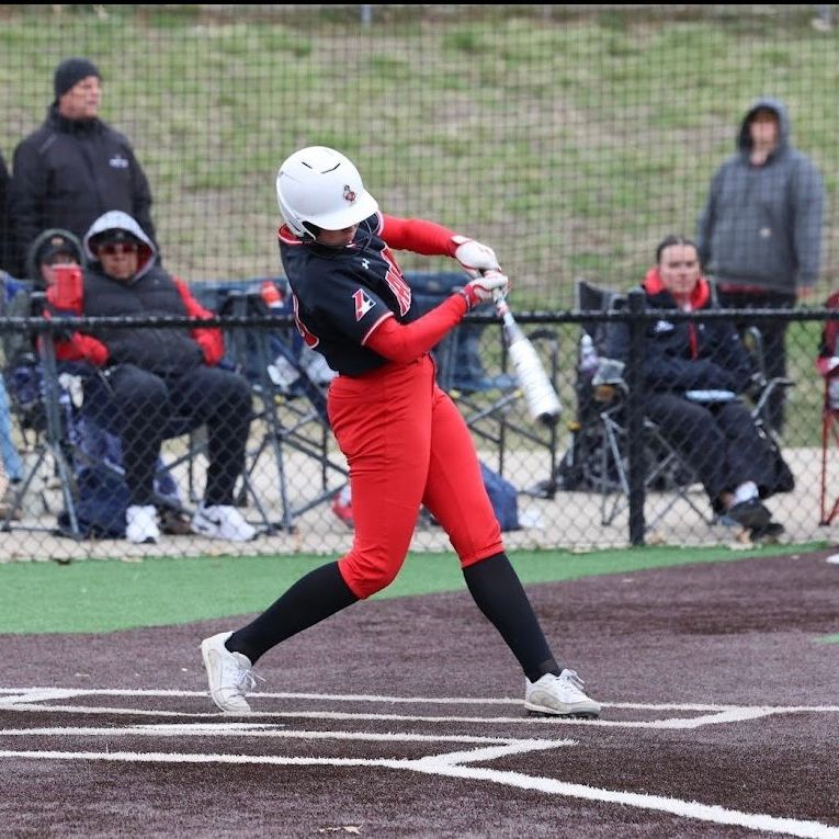 Softball player in red uniform swings bat at outdoor game.